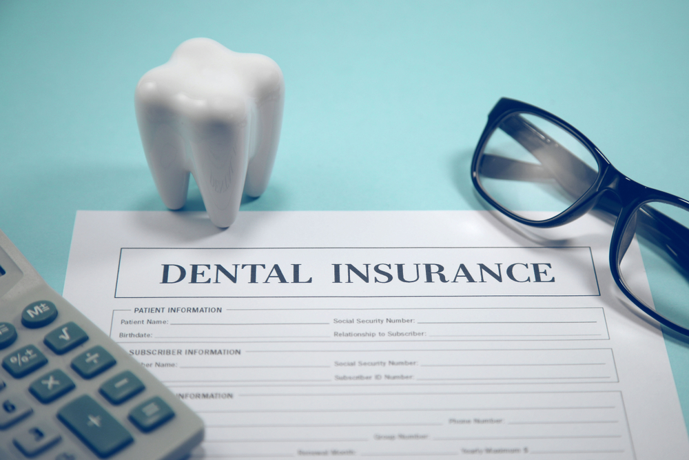 Dental insurance sheet next to tooth replica, glasses and calculator