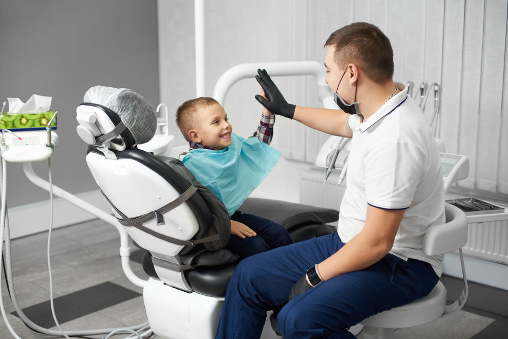 Young happy child sitting in dentist's chair giving a high five to the dentist