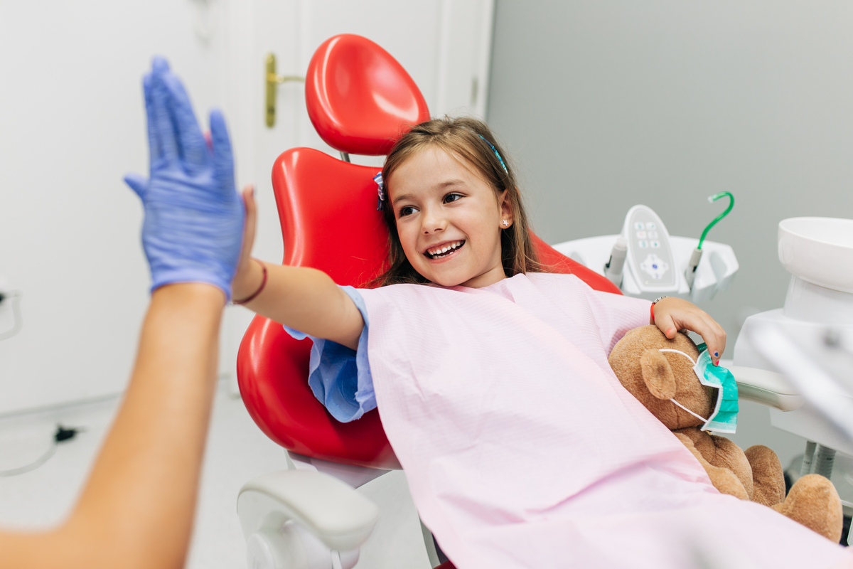 A child in a dentist's seat smiles and high-fives their dentist.